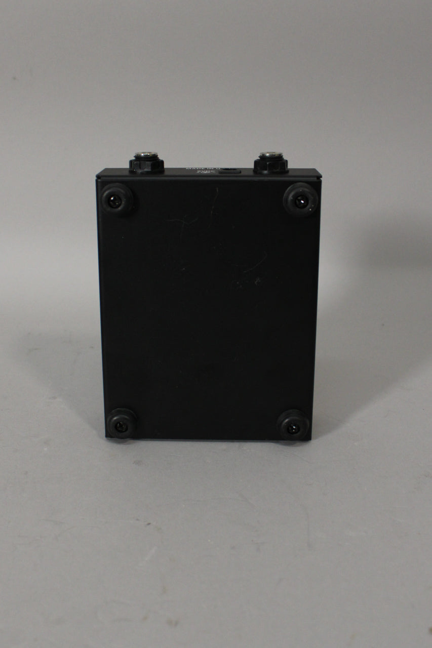 The black pedal is viewed from the rear, showing two input jacks, four rubber feet, and light surface scratches.