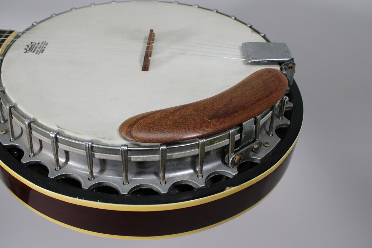 Close-up of the banjo's white head, showing the wooden armrest, chrome tension hooks, and dark brown rim with cream binding.