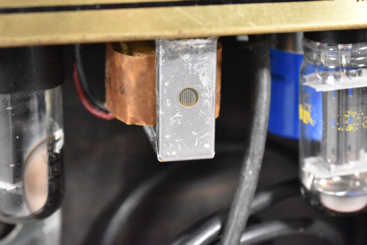 Close-up of internal components, showing a copper-wrapped transformer, a silver metal bracket with a circular vent, and two glass vacuum tubes.
