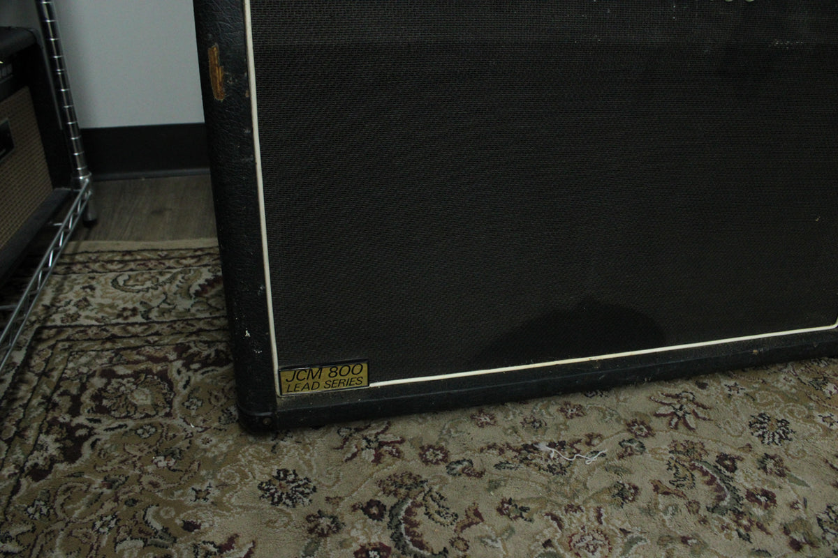 The black tolex cabinet is angled, showing the lower right corner and part of the grille cloth with a gold badge.