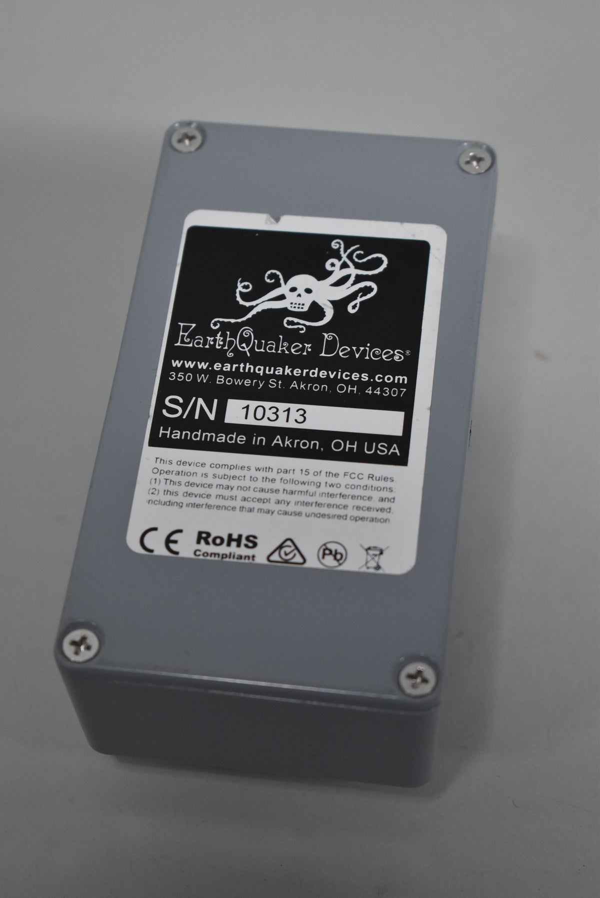 The gray pedal is viewed from above, showing the black and white serial number sticker on its top surface.