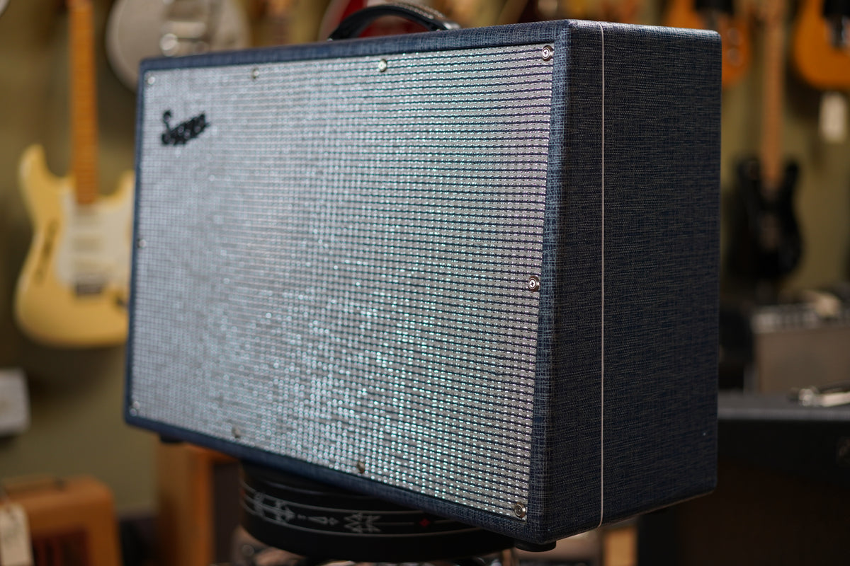 The dark blue tweed amp is angled right, showing its silver grille with a black logo and a white piping detail on the side.
