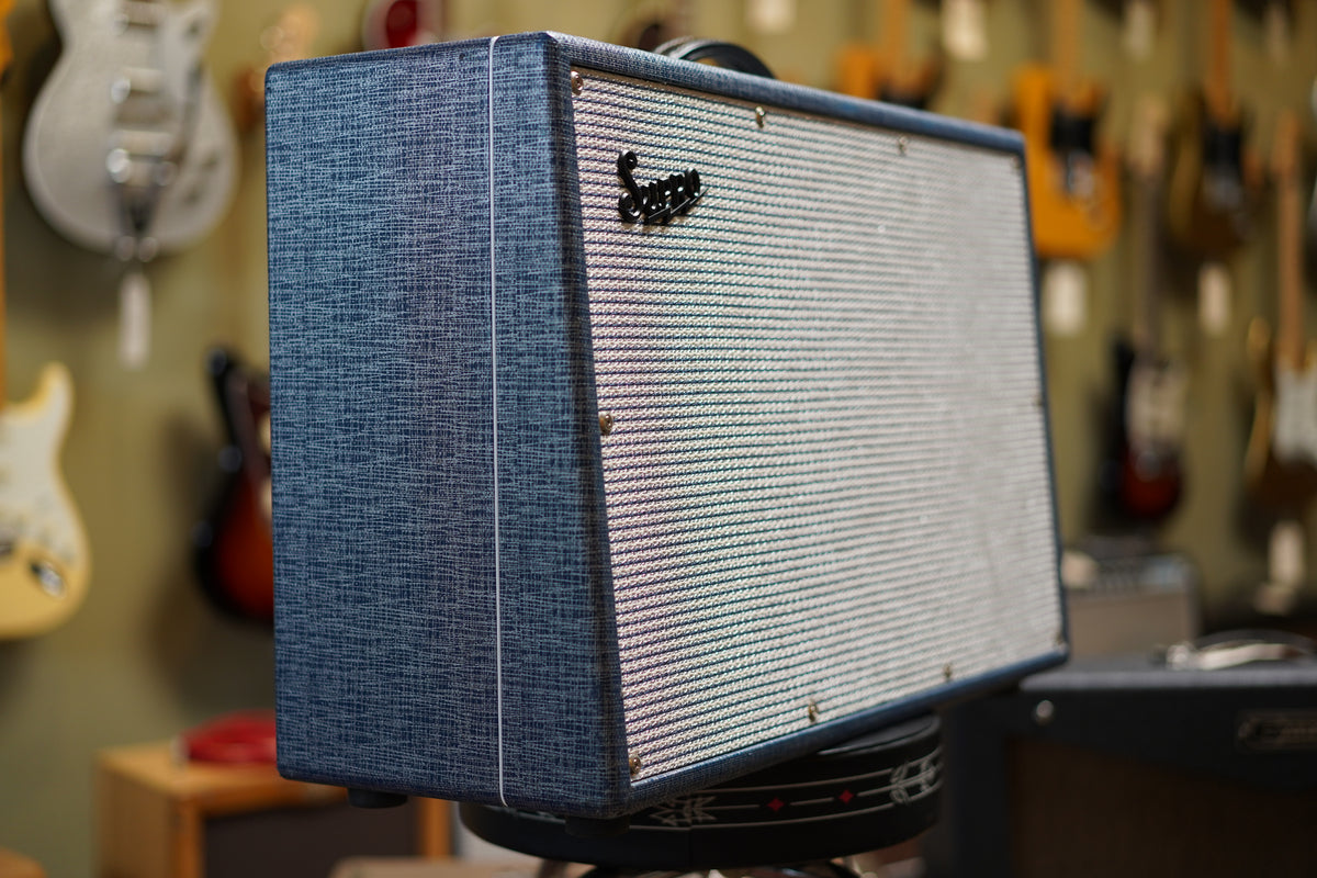 The blue-gray textured combo amp is angled right, showing its side and the light gray grille with a black logo.