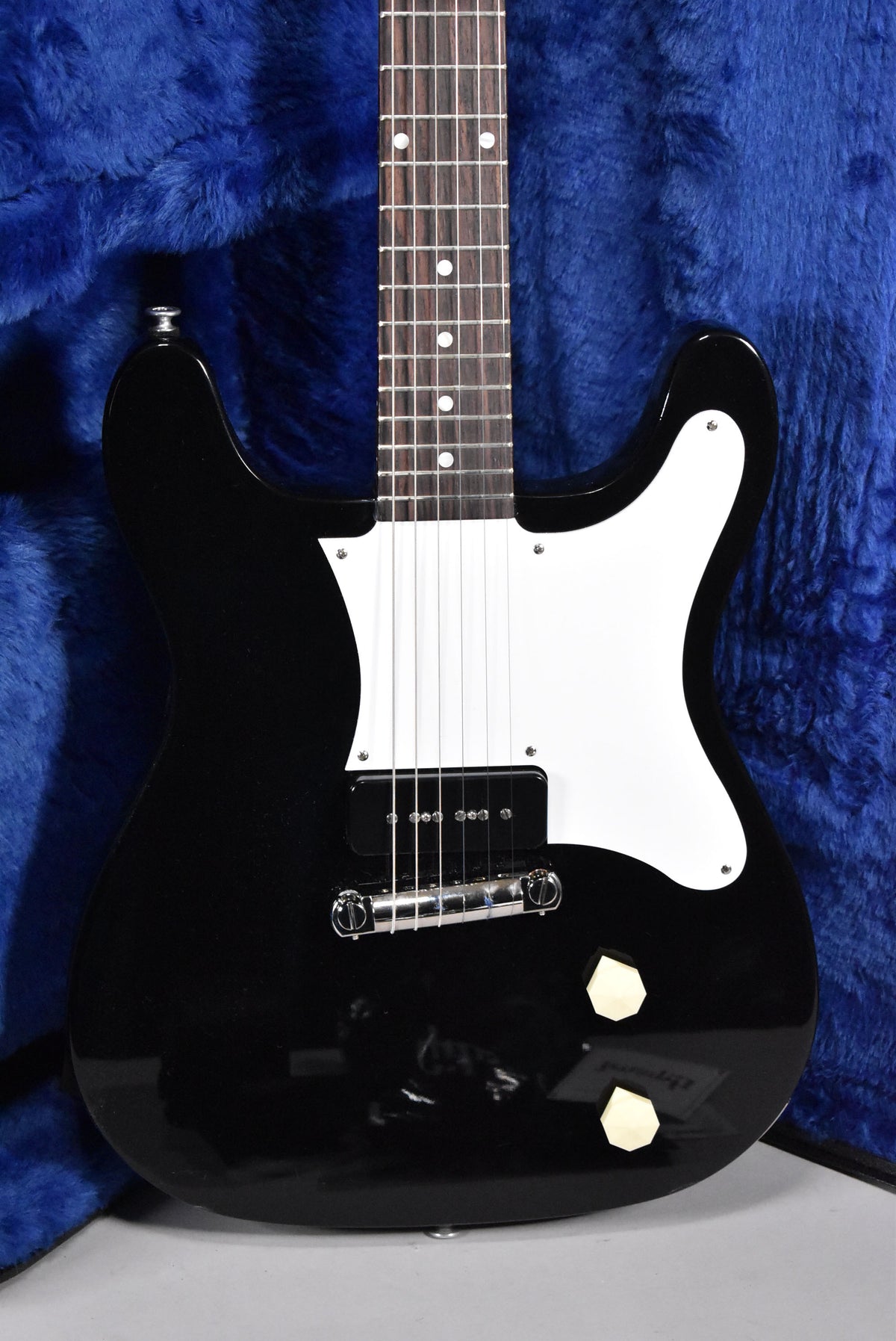 Full-frame view of a glossy black electric guitar with a white pickguard, single P90 pickup, and two cream-colored control knobs.