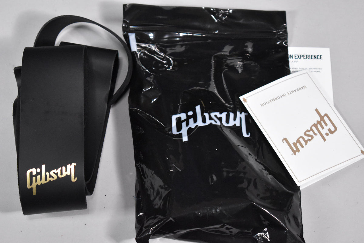 A black leather strap with a gold logo, a black plastic bag, and two white cards with gold lettering are shown from above.