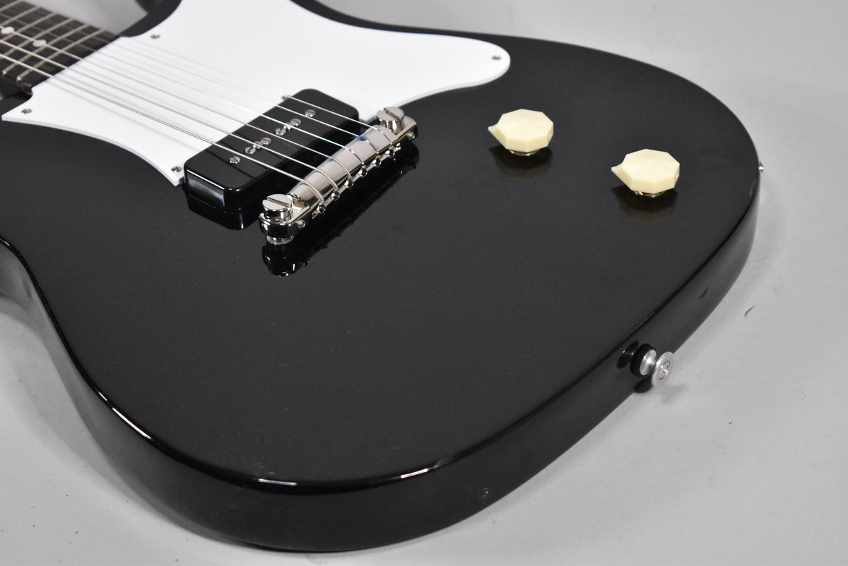 Close-up of the glossy black body, showing a white pickguard, chrome bridge, black P90 pickup, and two cream control knobs.