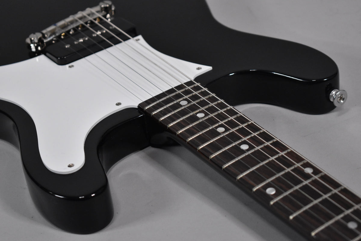Close-up of the glossy black guitar body, white pickguard, chrome bridge, and dark fretboard with white dot inlays.