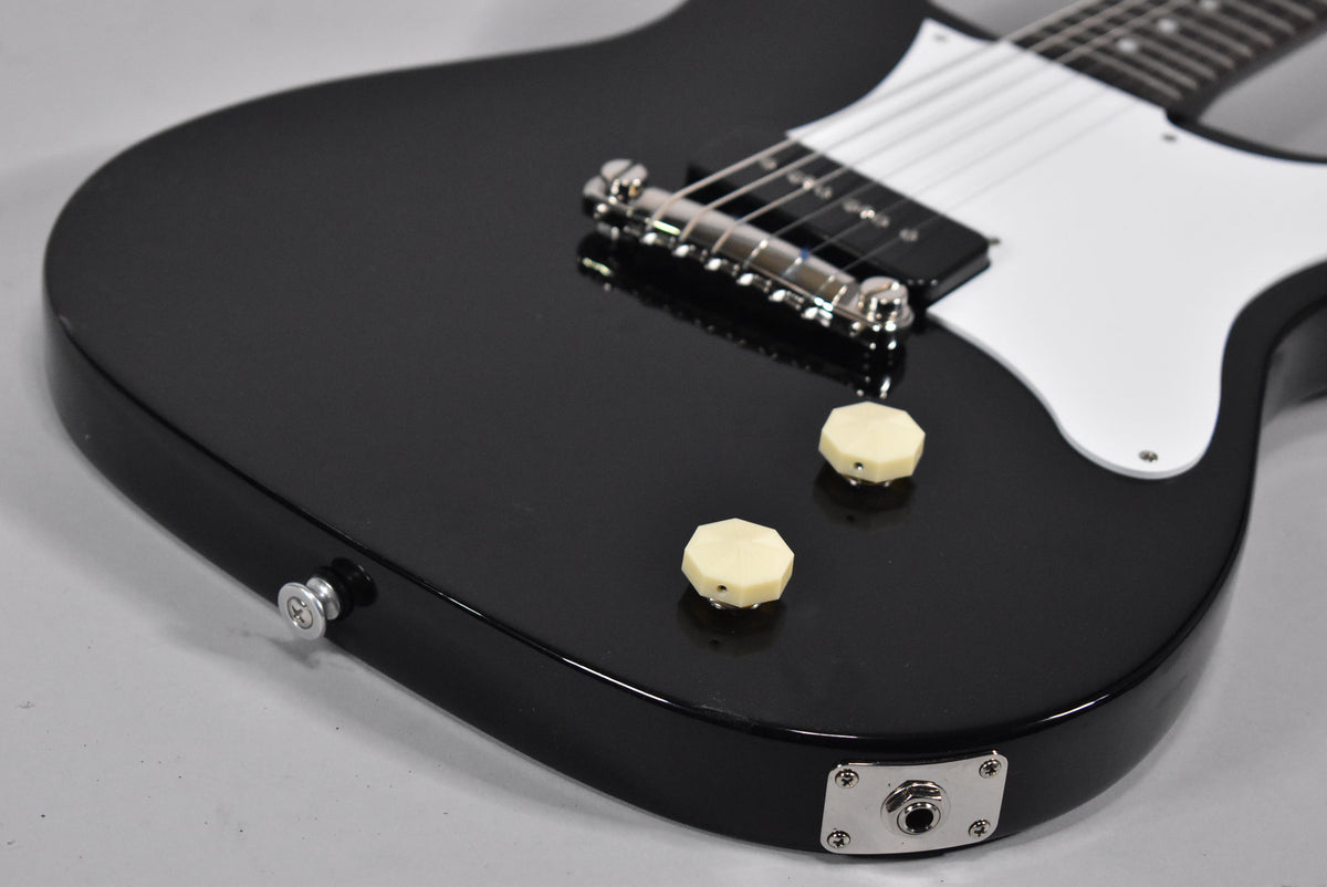 Close-up of the glossy black body, showing the white pickguard, chrome bridge, two cream octagonal knobs, and output jack.