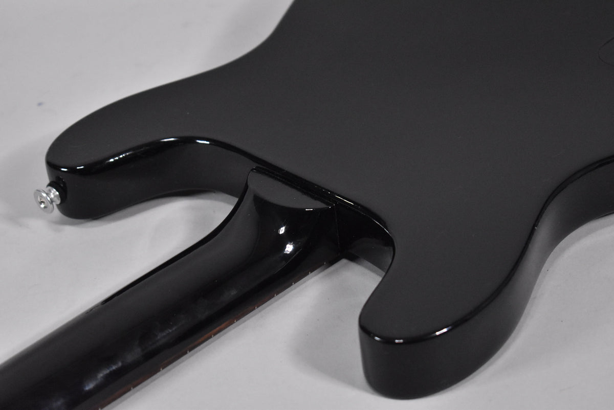 The back of the guitar, showing the glossy black neck heel and lower horn, with a matte black body and chrome strap button.