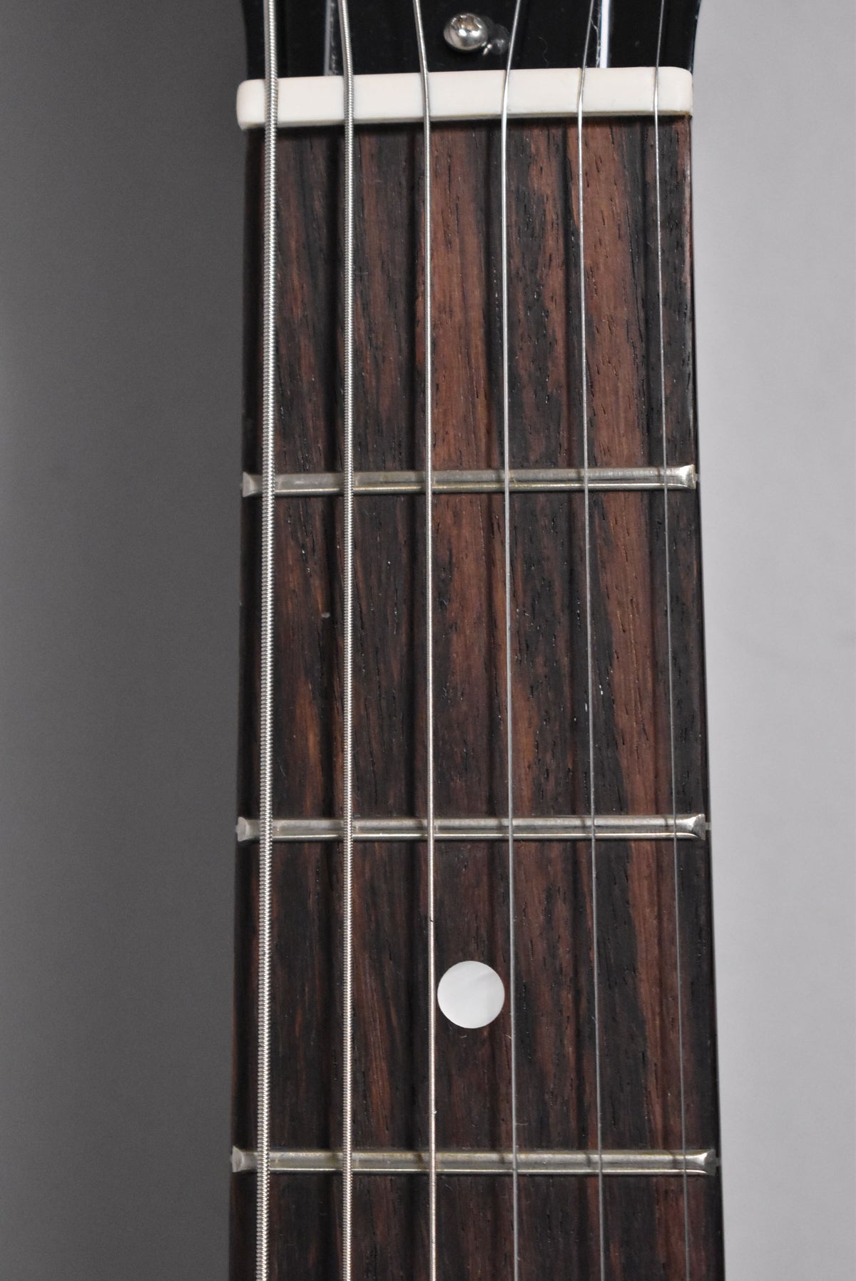 Close-up of the dark brown fretboard with prominent wood grain, showing a white nut, four frets, and a single white dot inlay.