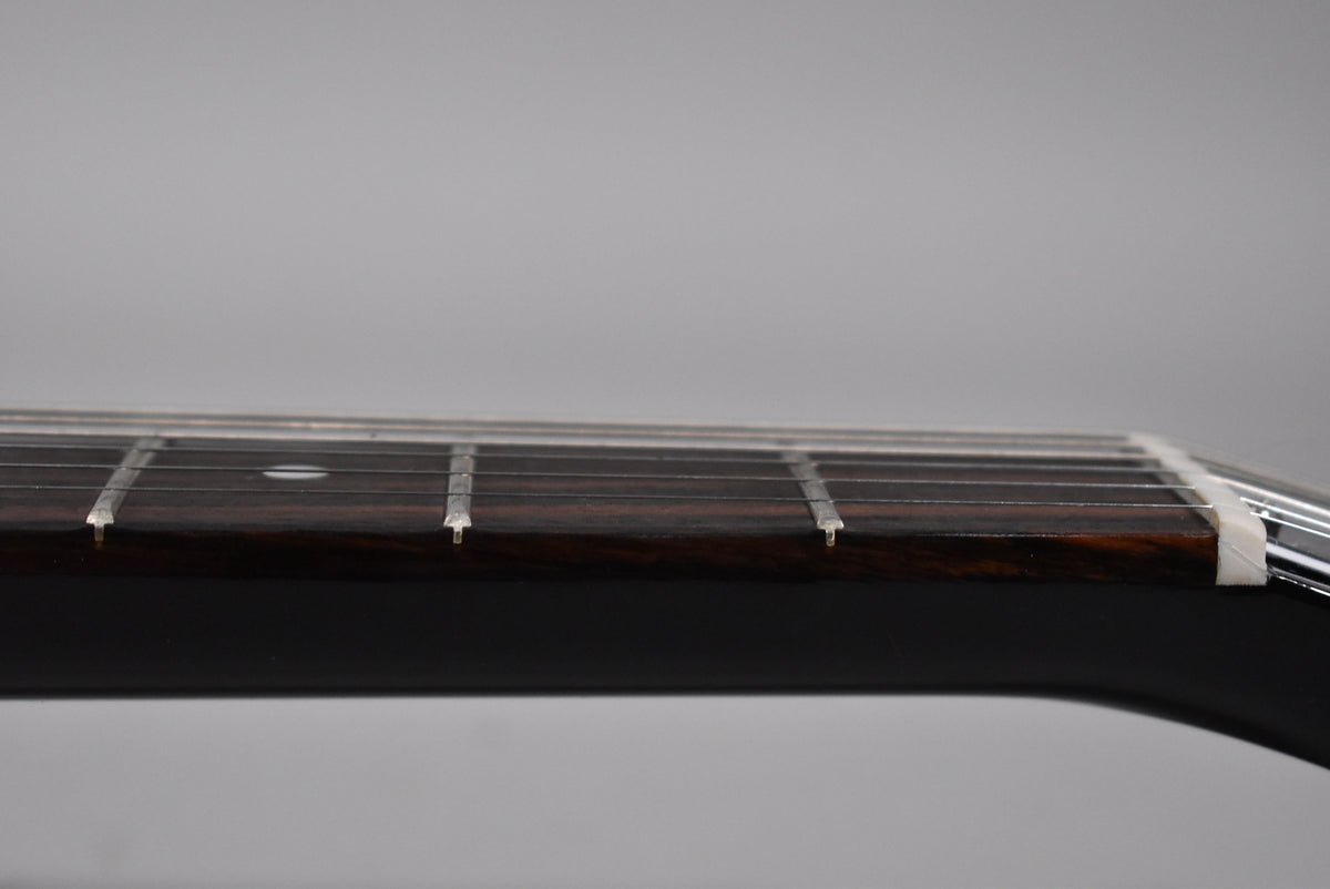 Close-up of the dark fretboard and frets, with a white nut visible on the right and a single dot inlay on the 7th fret.
