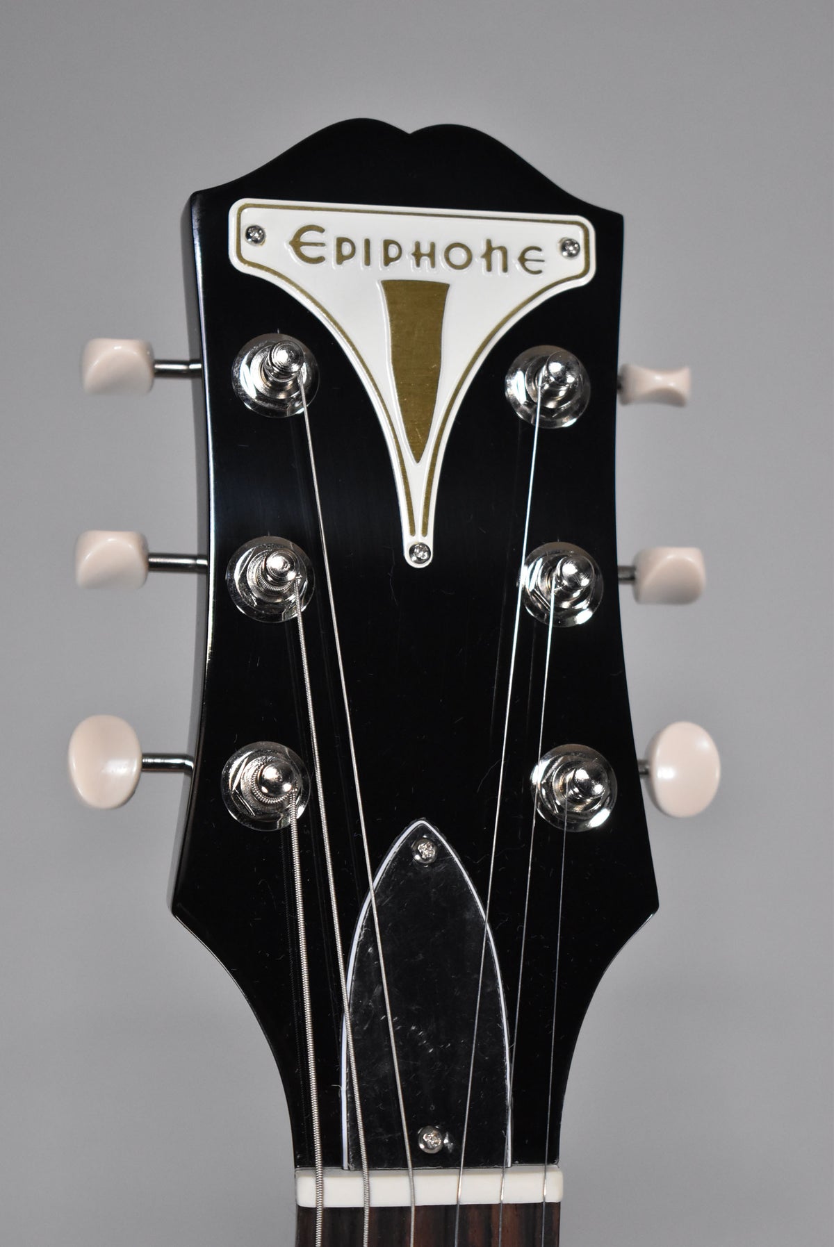 Close-up of the glossy black headstock with white and gold logo, six chrome tuners with cream buttons, and a clear truss rod cover.