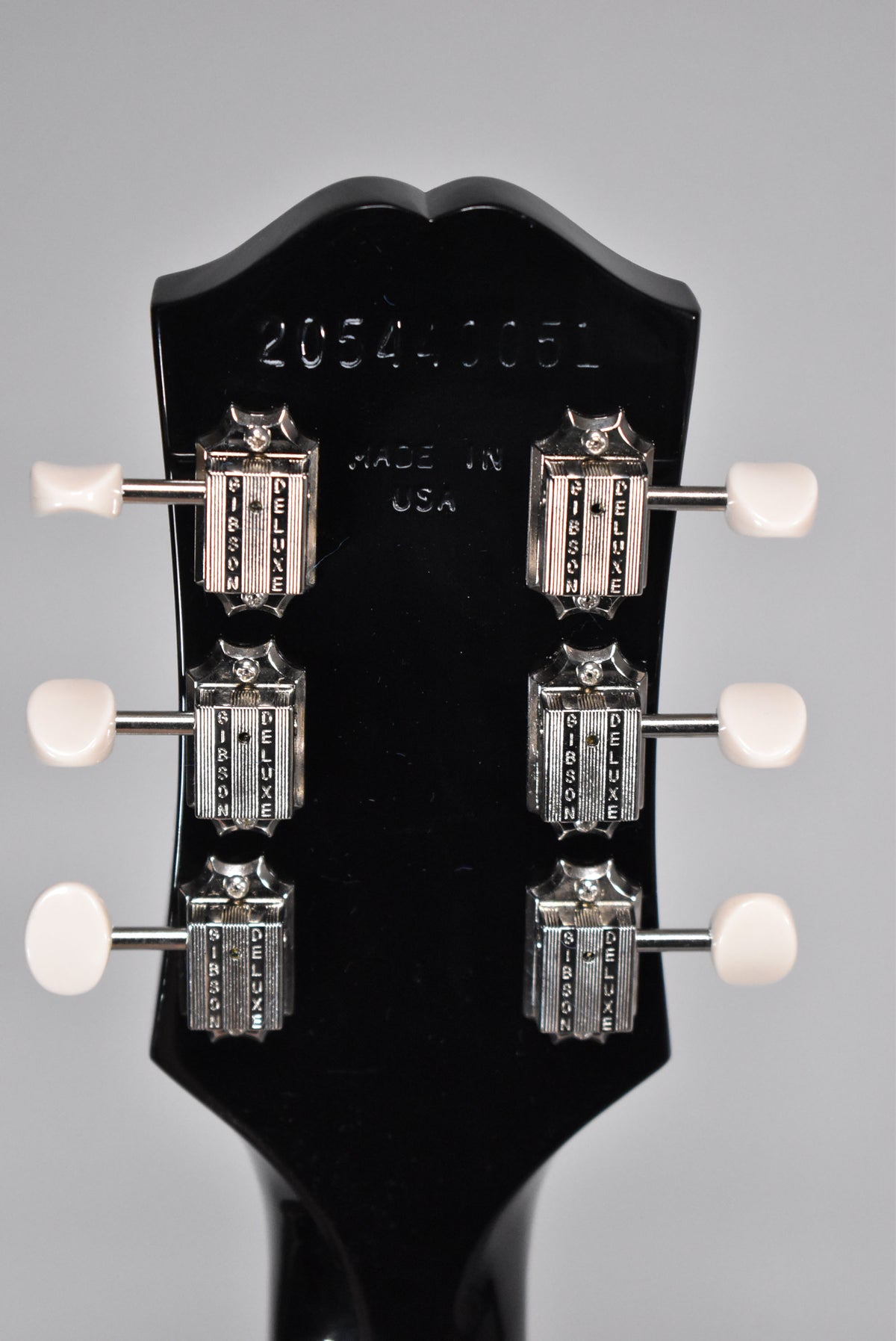 The back of the glossy black headstock shows six chrome tuners with white buttons, arranged 3x3, with a serial number at the top.