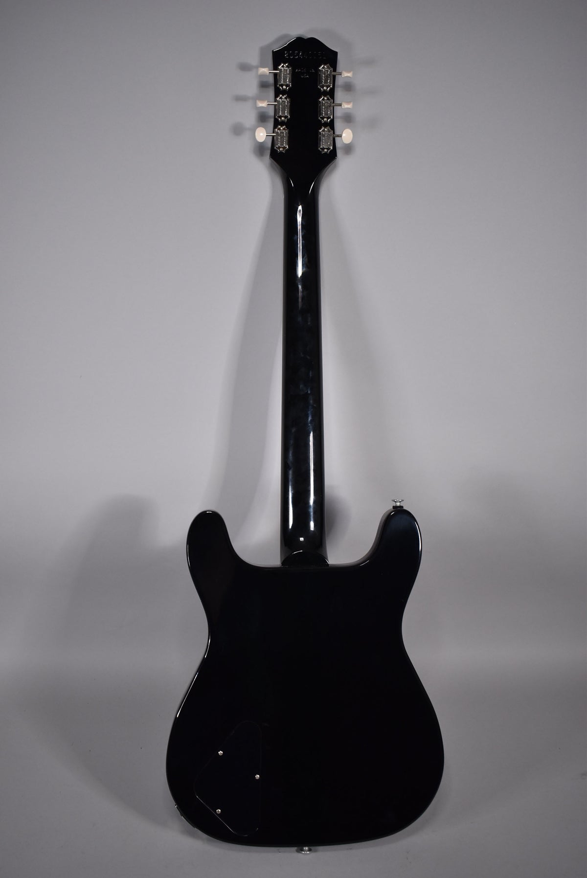 Full rear view of a glossy black electric guitar, showing the headstock with six white-button tuners and a control cavity cover.
