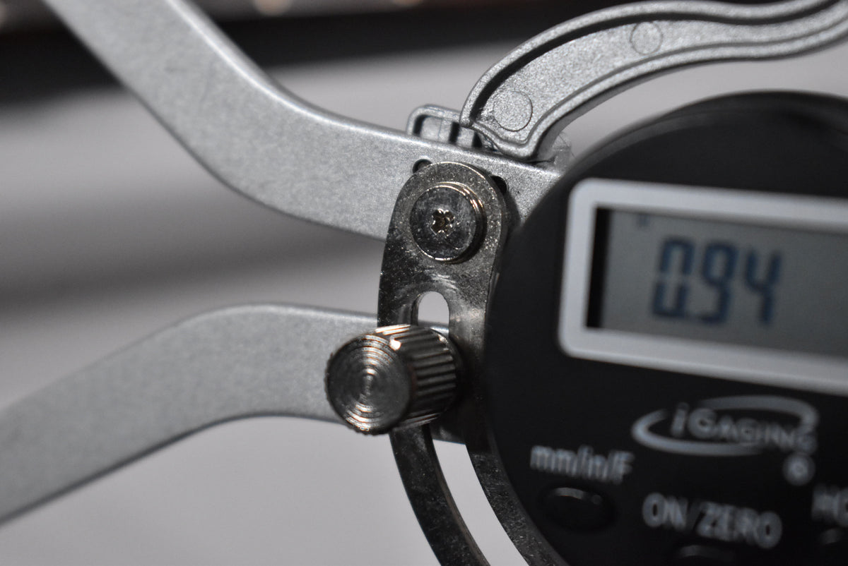 A close-up of a digital caliper measuring the guitar's nut width, displaying "0.94" on its screen.