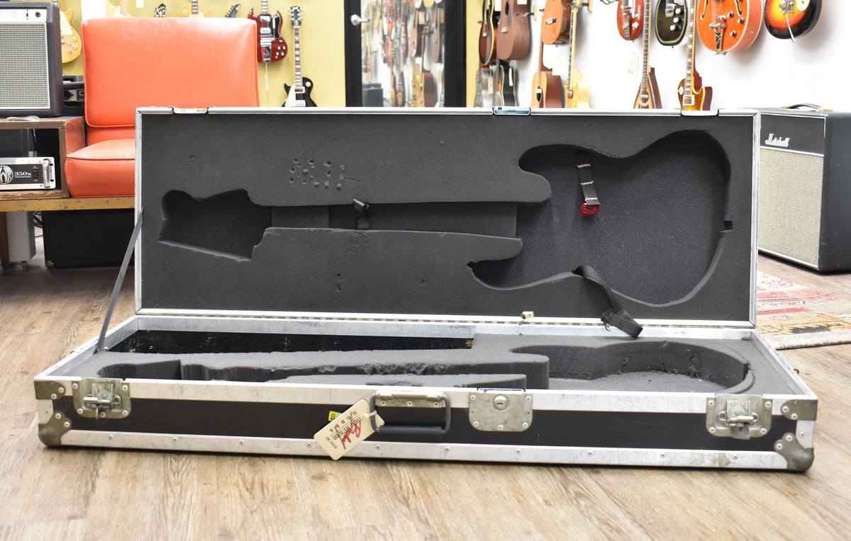 Open black flight case with silver hardware, showing a custom-cut black foam interior with a bass guitar shape.