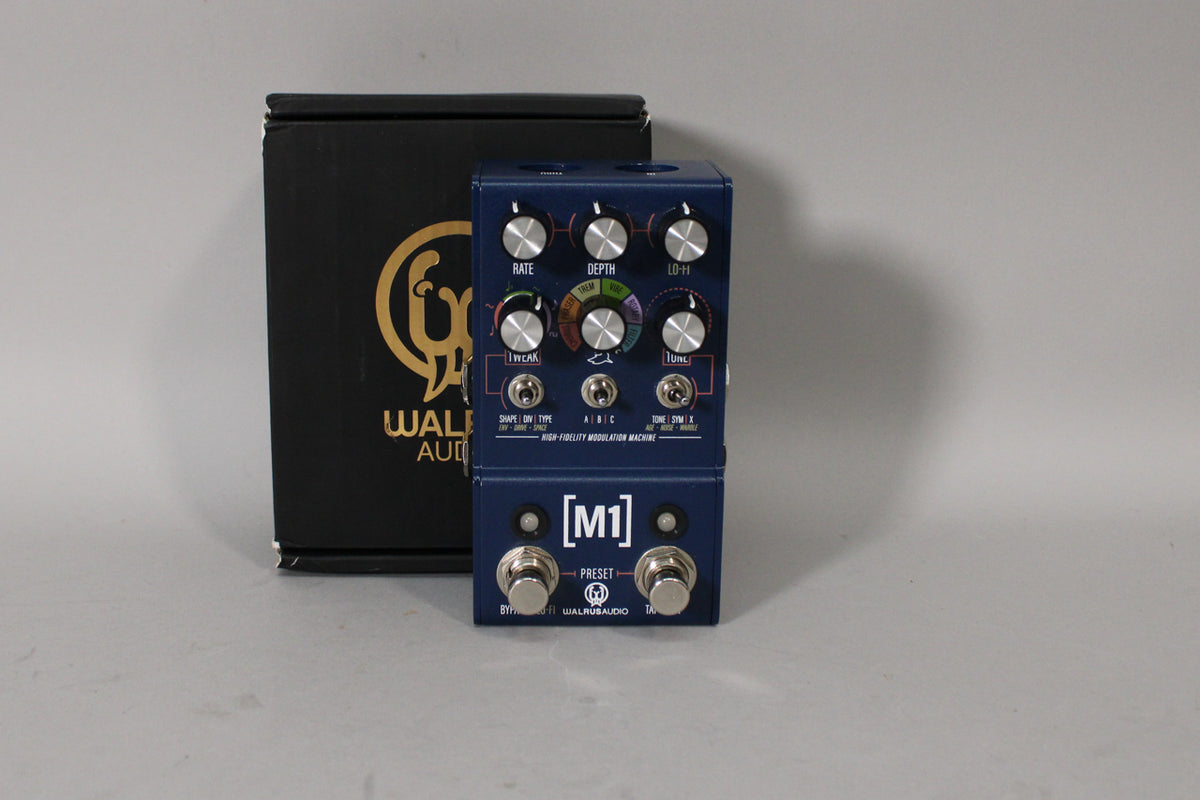 A dark blue guitar pedal with two footswitches and nine silver knobs, shown at a slight angle with its black box behind it.