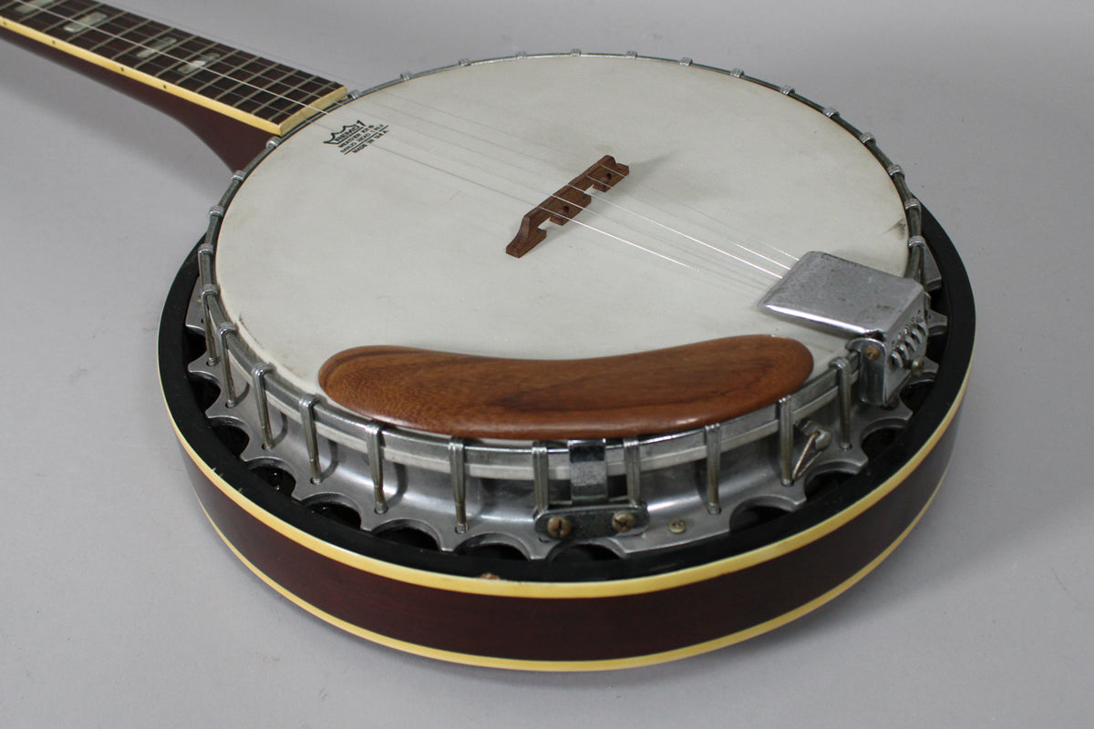 The banjo's dark brown body, white head, and chrome hardware are visible from an overhead angle, showing a wooden armrest.