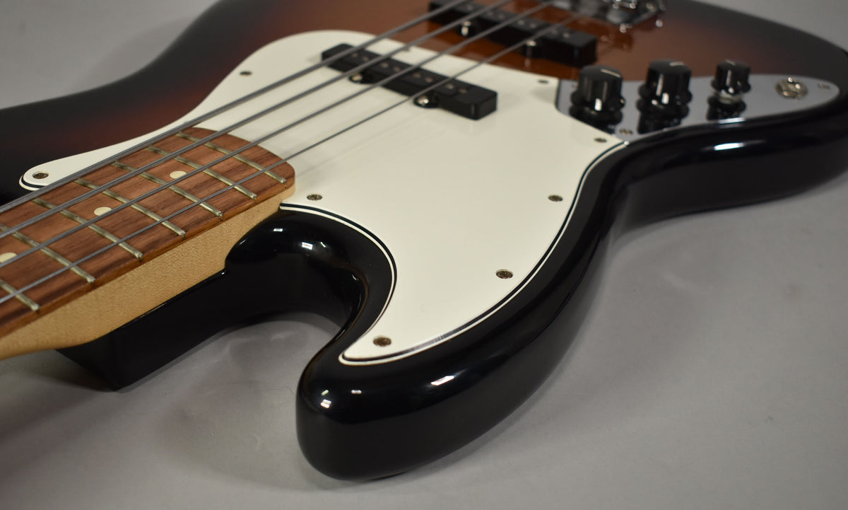 Close-up of the bass body, showing the glossy 3-tone sunburst finish, white pickguard, two pickups, and three control knobs.