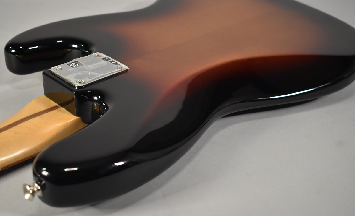 Close-up of the bass guitar's glossy 3-Tone Sunburst body, showing the neck plate and strap button on the lower horn.
