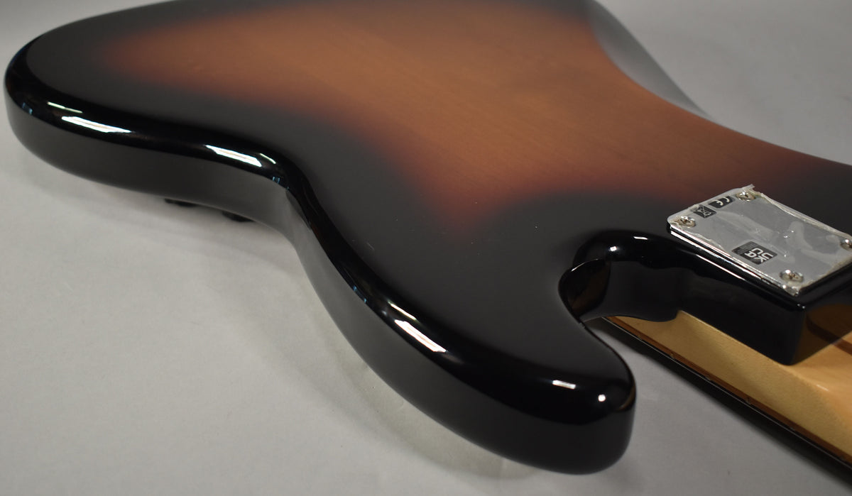 Close-up of the bass guitar's lower body, showing the glossy 3-tone sunburst finish and the chrome neck plate.