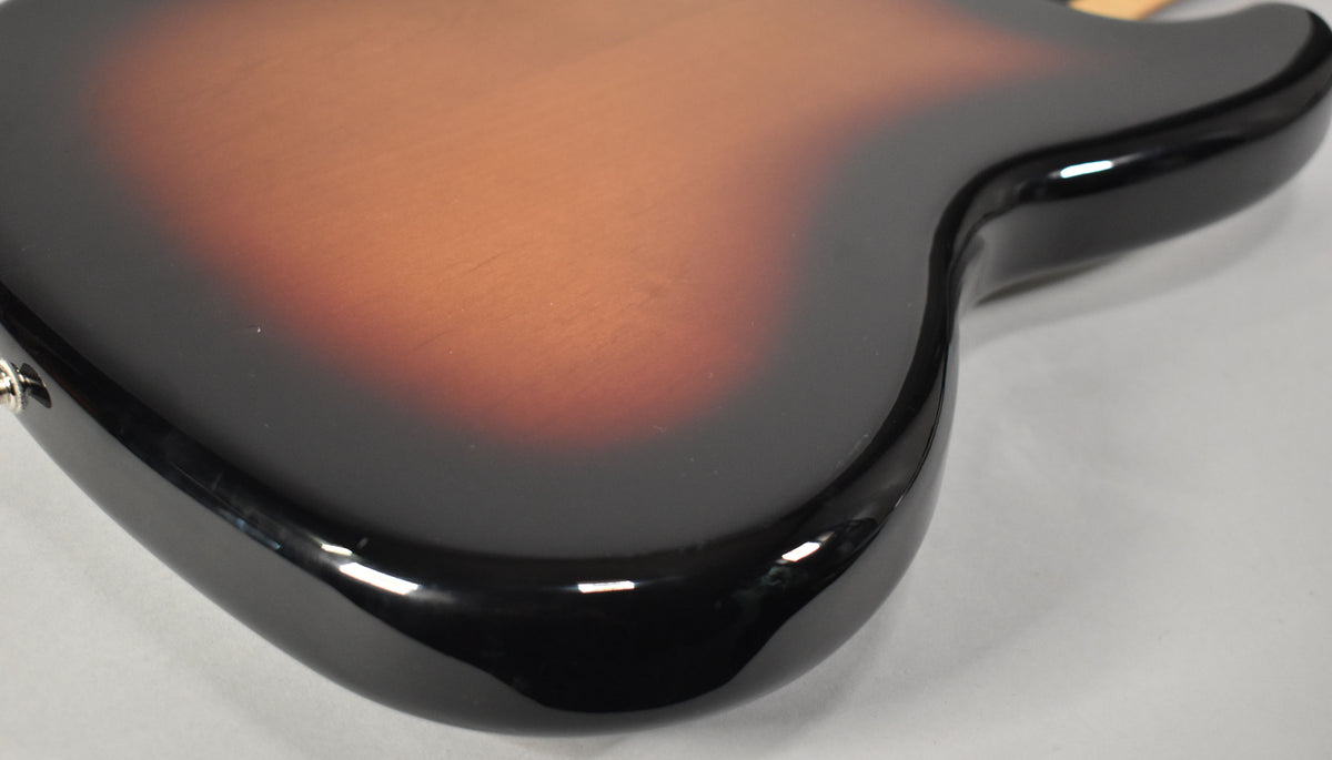 Close-up of the bass guitar's lower body, showing the glossy 3-Tone Sunburst finish with a small ding on the dark brown section.