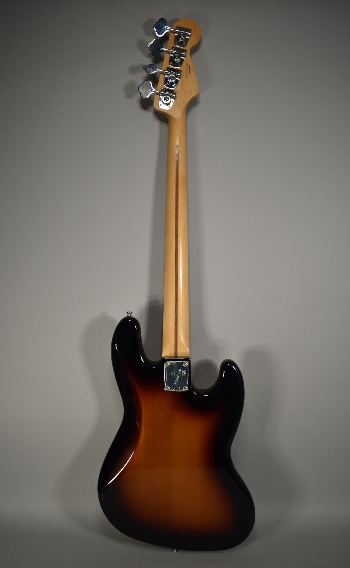 The back of the 3-Tone Sunburst Jazz Bass shows a glossy finish, a maple neck, and chrome tuners on the headstock.