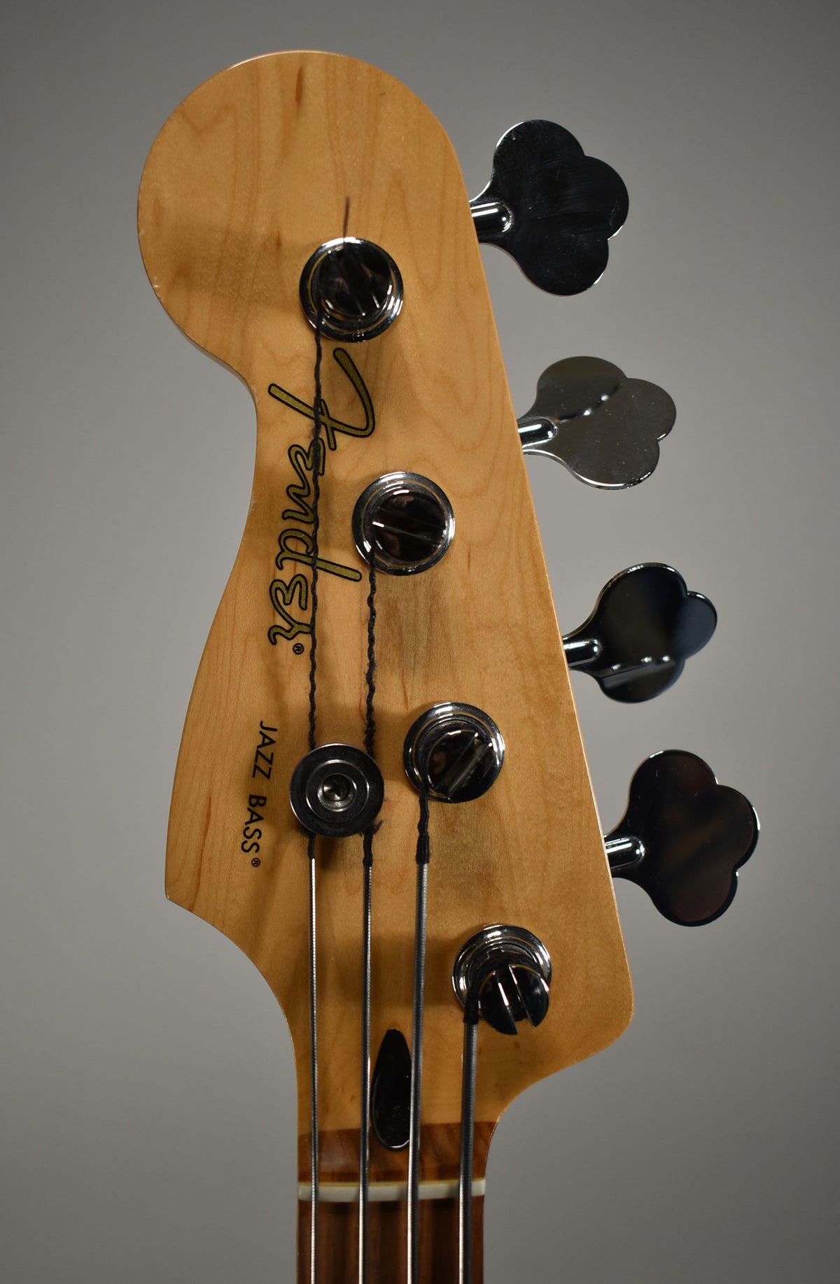 Close-up of a light wood headstock with four chrome clover-leaf tuners and a black string tree, angled slightly left.