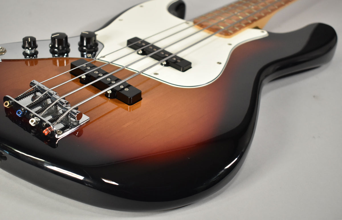 Close-up of the bass body, showing the glossy 3-tone sunburst finish, chrome bridge, black pickups, and white pickguard.