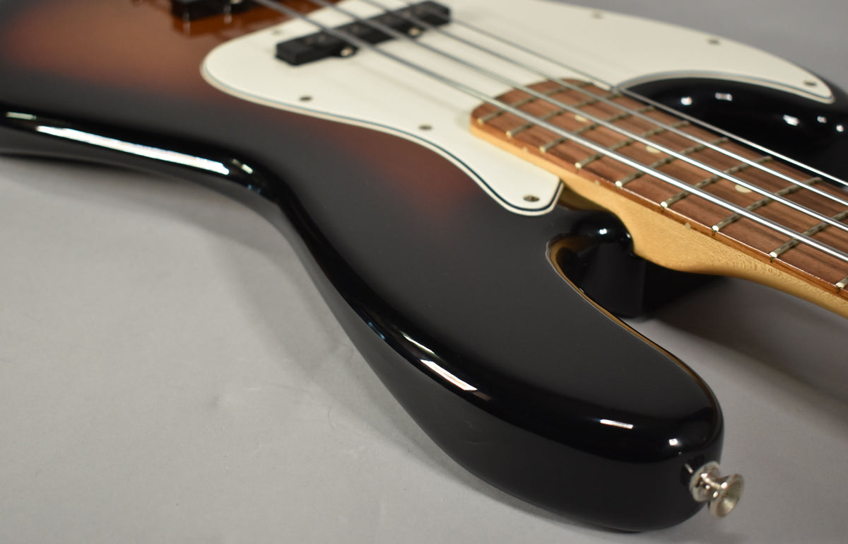 The lower body of a sunburst bass, showing the glossy black finish, white pickguard, and part of the fretboard.