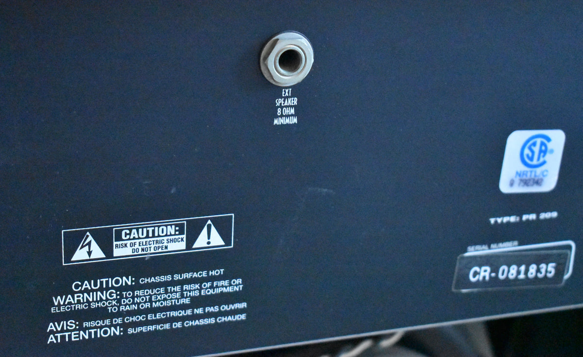 Close-up of the amp's black rear panel, showing an external speaker jack, safety warnings, and serial number CR-081835.