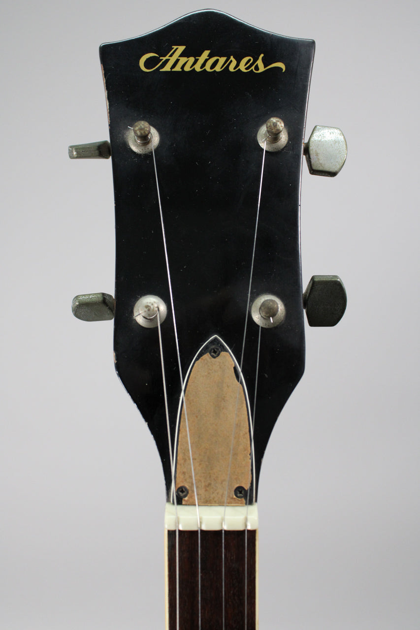 Close-up of the black headstock with gold lettering, showing four tarnished tuners, a worn truss rod cover, and a white nut.