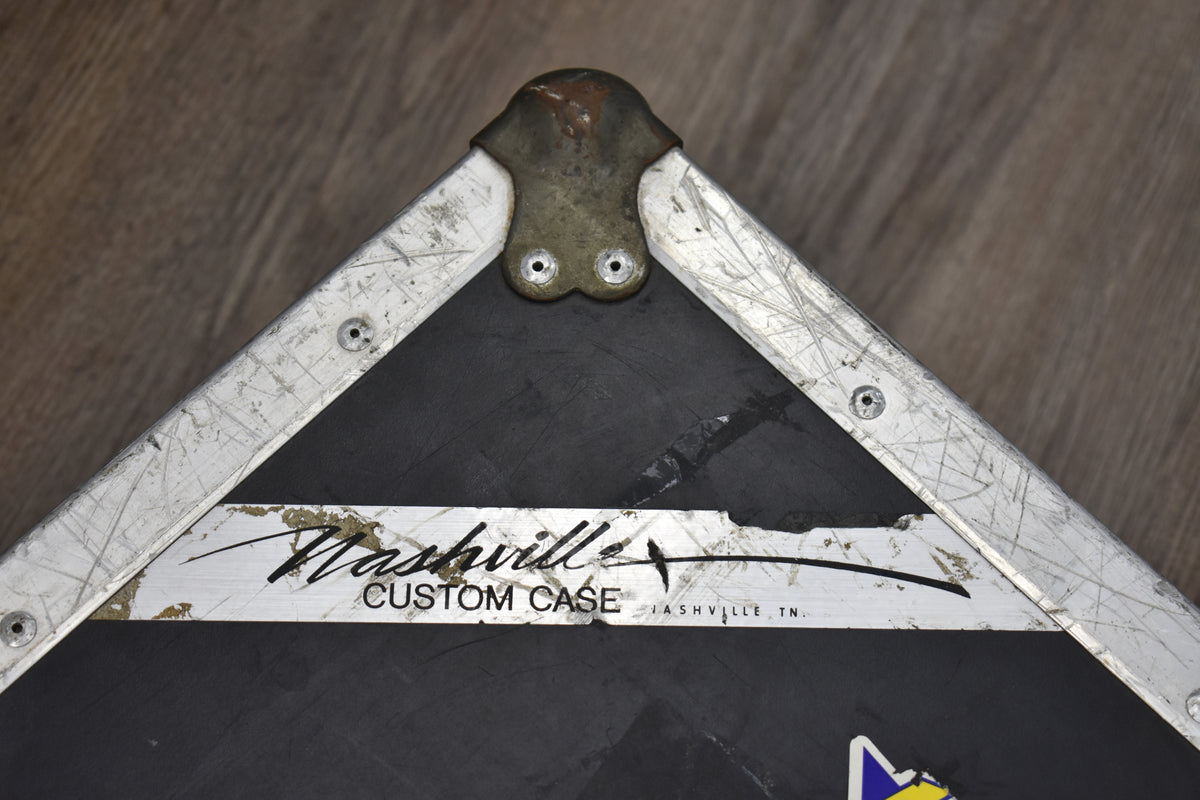 Top-down view of a black flight case corner, showing a worn brass corner cap and heavily scratched aluminum edging.