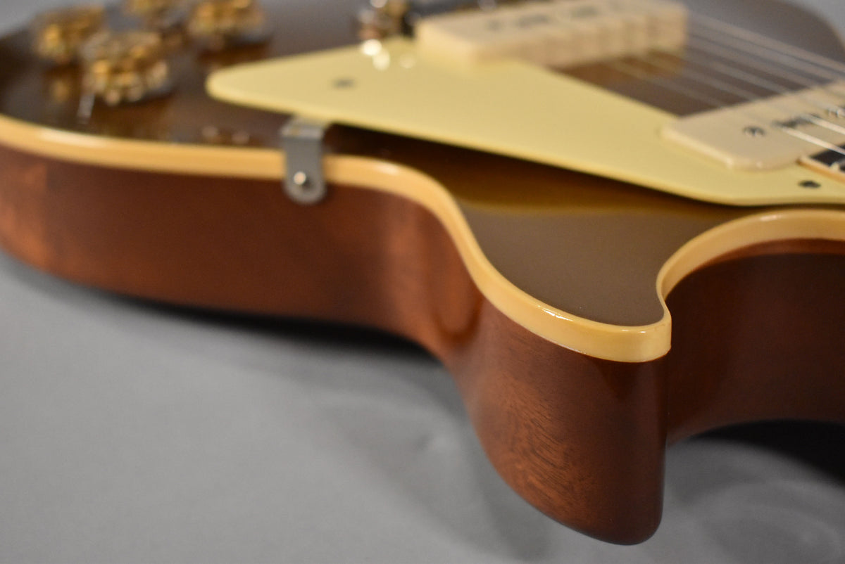 The upper bout of a goldtop guitar, showing the dark mahogany back and sides, cream binding, and a cream pickguard.