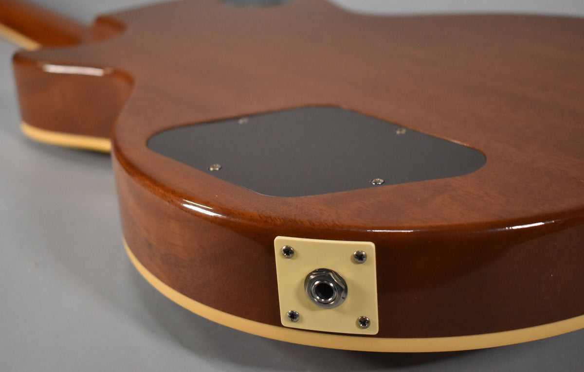 The guitar's mahogany back and sides are visible, with a black control cavity cover and a cream-colored output jack plate.
