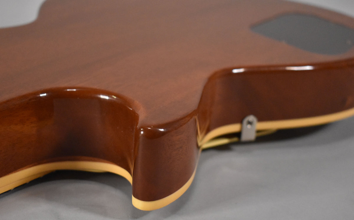 The guitar's dark brown back and sides are visible, with cream binding along the edges and a strap button near the cutaway.