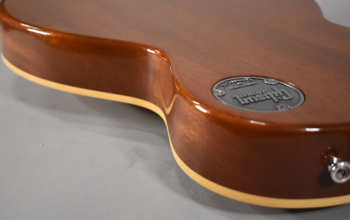 The back of a glossy brown guitar body is angled, showing cream binding and a silver circular medallion.