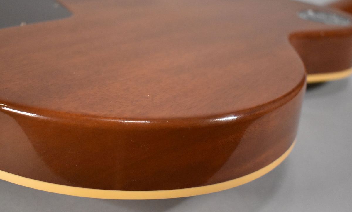 Close-up of the guitar's lower bout, showing the dark brown back and sides with a glossy finish and cream binding.