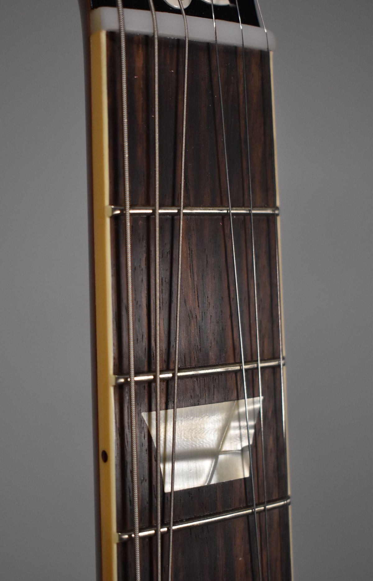 Close-up of the dark rosewood fretboard with trapezoid mother-of-pearl inlay, cream binding, and nickel frets.