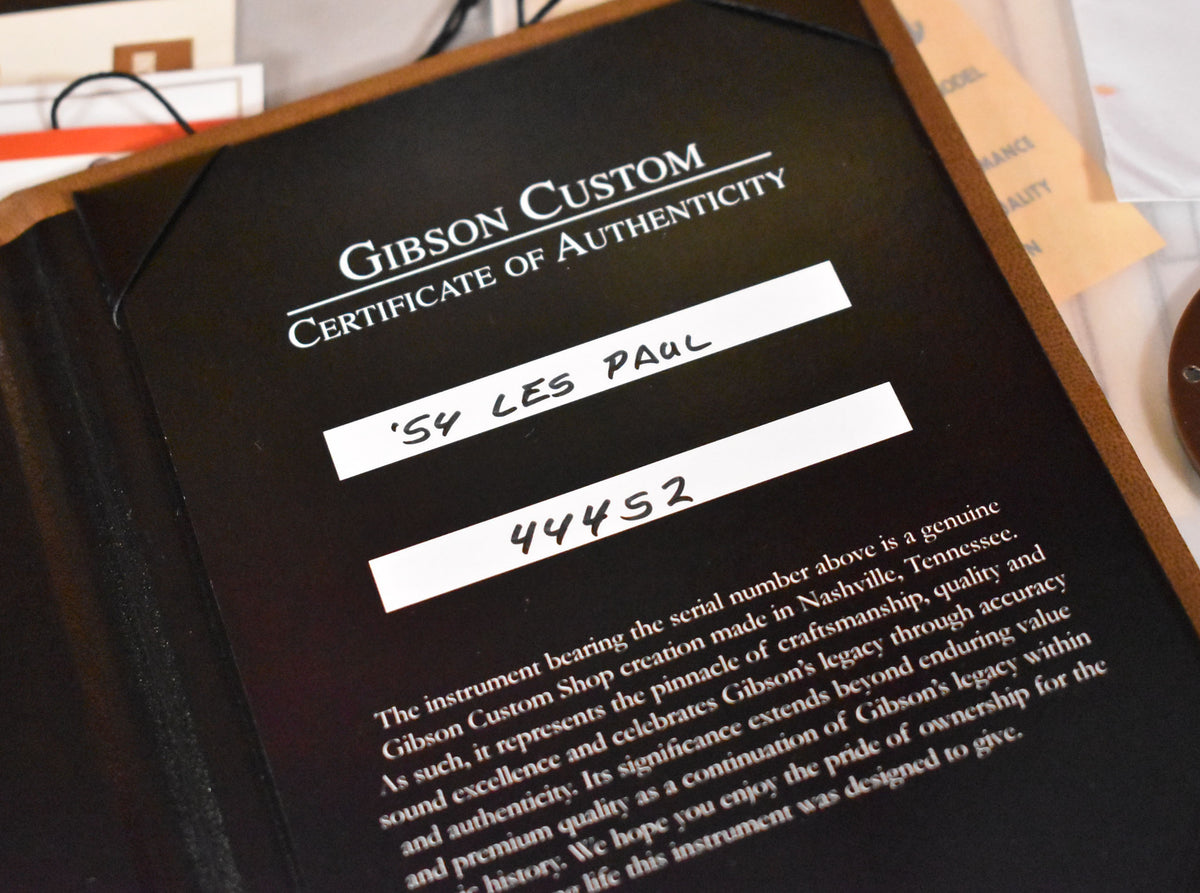 Close-up of a black Gibson Custom Certificate of Authenticity, with " '54 LES PAUL" and "44452" handwritten on white labels.