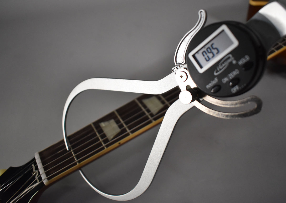 A digital caliper measures the guitar's nut width at 0.95, with the dark fretboard and trapezoid inlays visible.