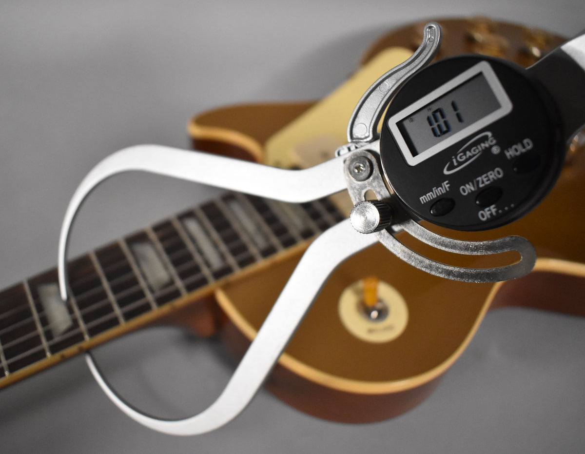 A digital caliper measures the guitar's fretboard, showing "1.01" on its screen, with the Goldtop body blurred in the background.