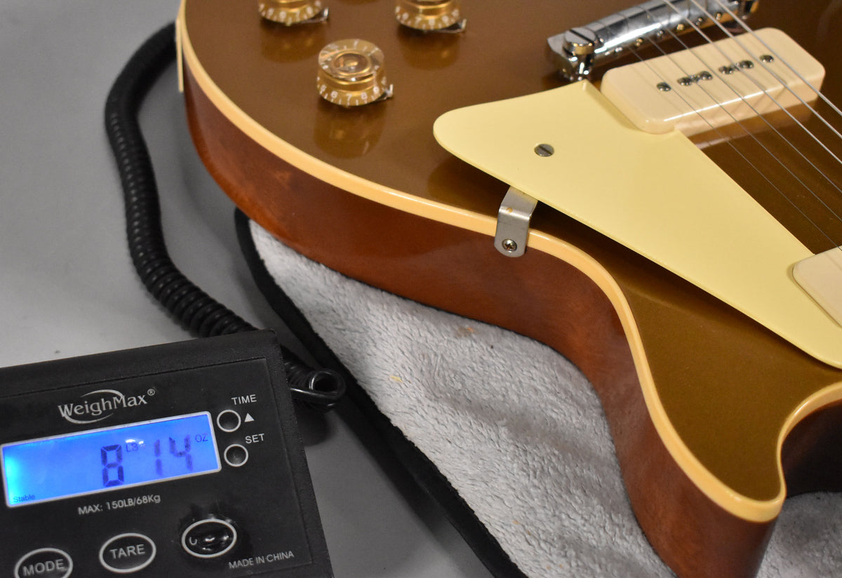 The goldtop guitar body is angled, showing the cream pickguard, P90 pickup, and a scale displaying "8.14" lbs.
