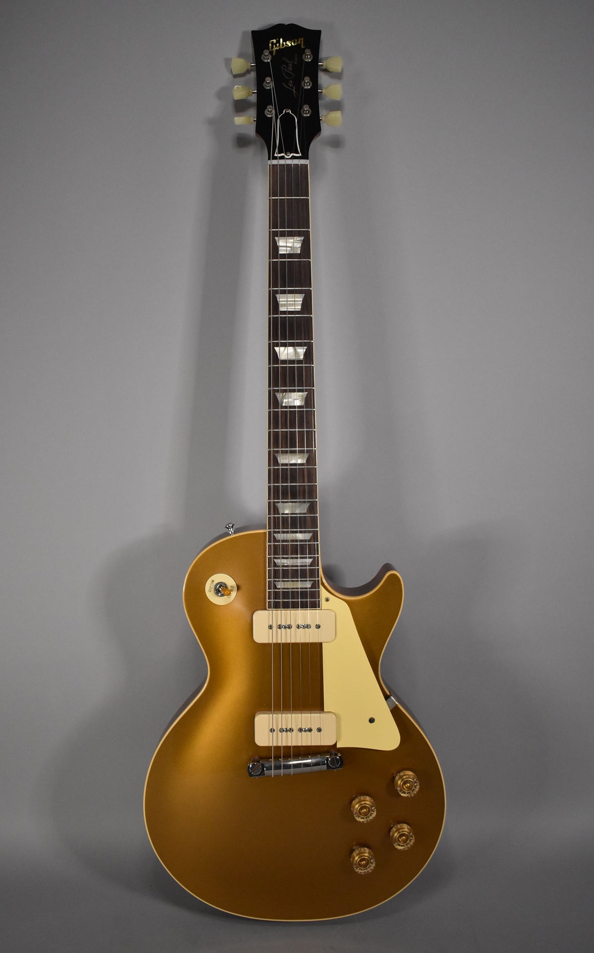 Full-length view of a goldtop electric guitar with cream P90 pickups, a trapeze tailpiece, and four gold control knobs.