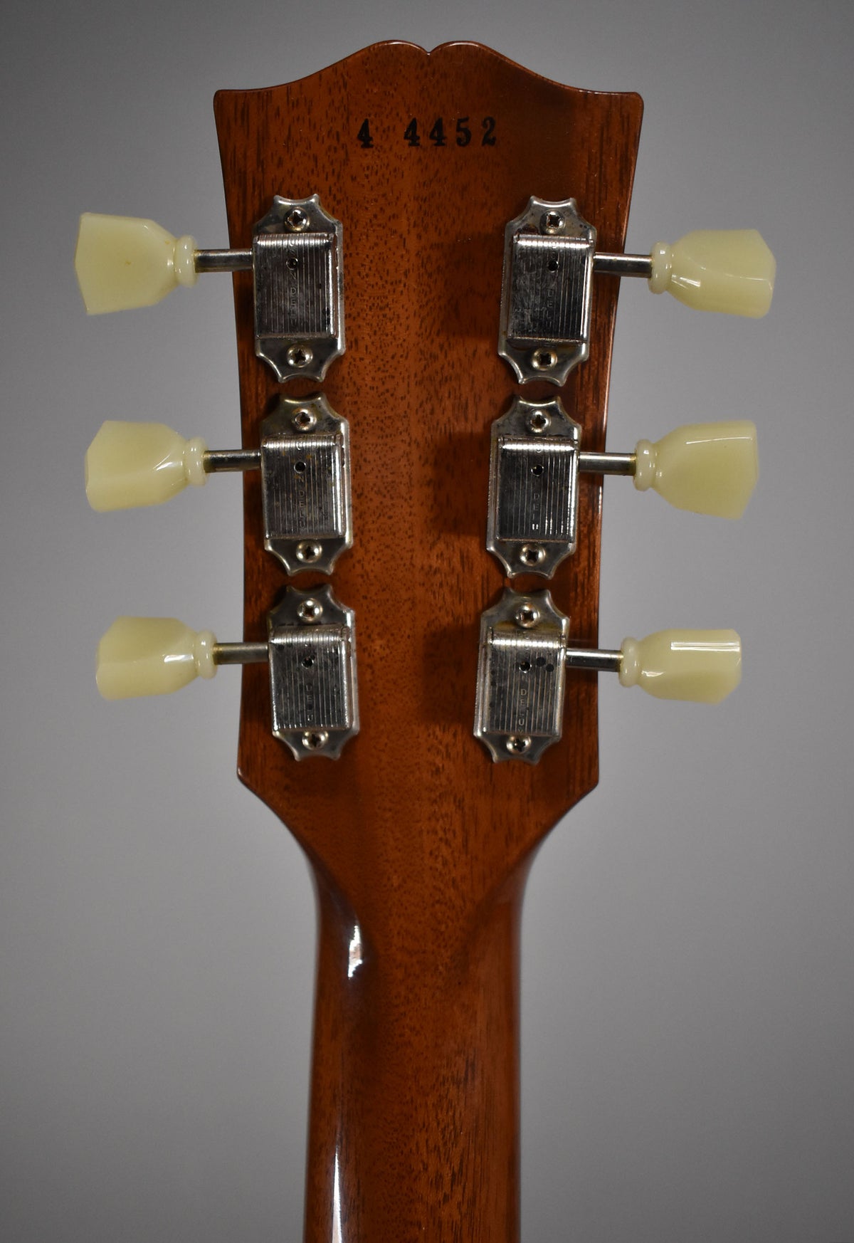 The back of a guitar headstock and neck, showing six cream-colored tuning pegs and chrome tuners on a glossy brown wood finish.