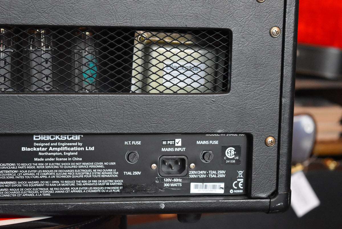 The amp's textured black rear panel shows a mesh-covered tube compartment, power input, and fuse holders, with minor scuffs on the bottom edge.