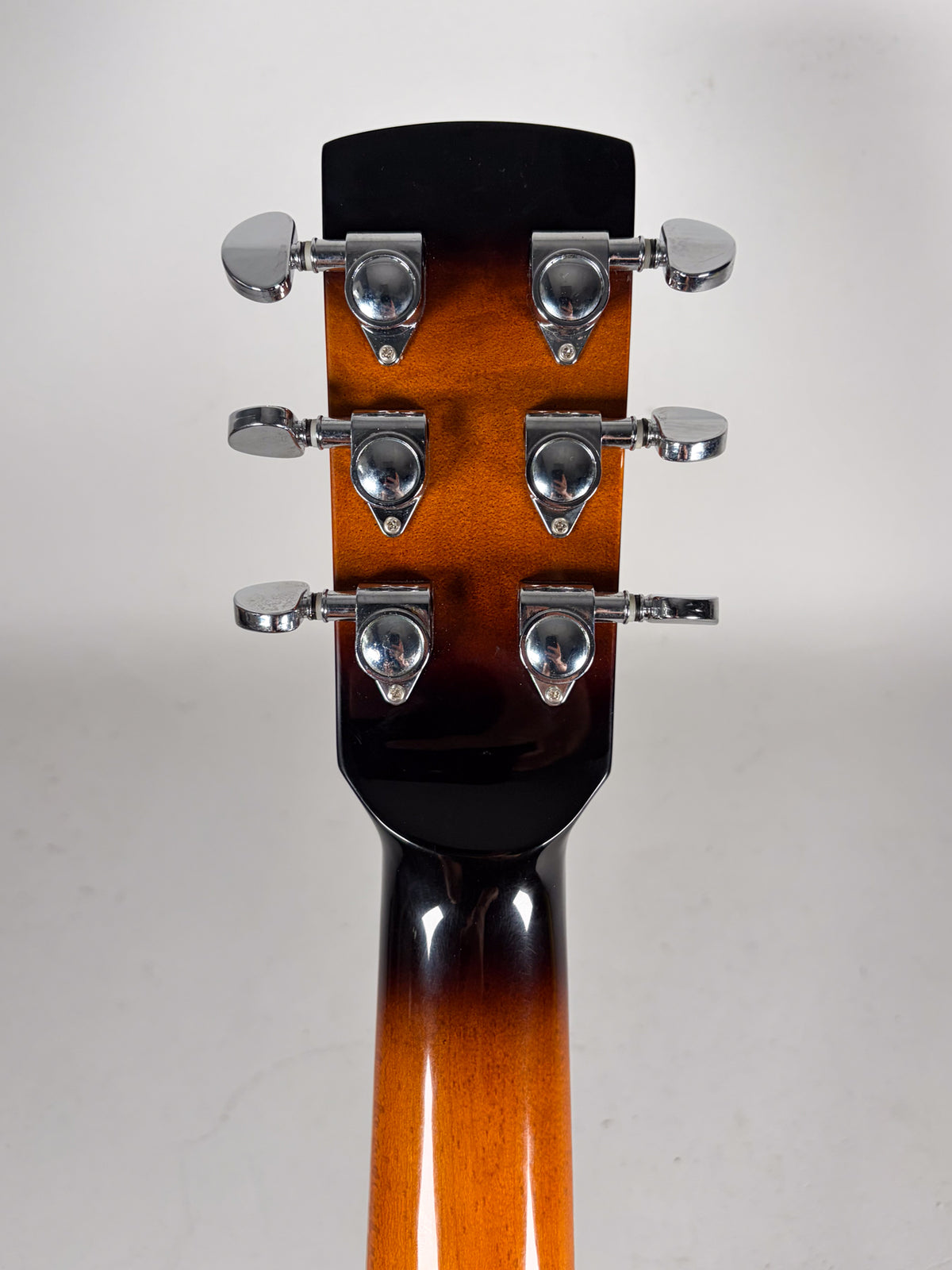 The back of a sunburst resonator headstock and neck, showing six chrome tuners with oval buttons.