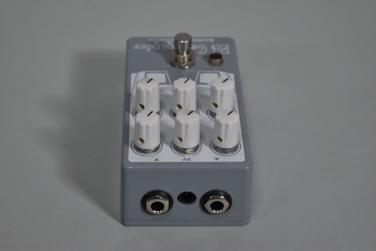 The gray pedal is angled slightly, showing its six white knobs, a silver footswitch, a red LED, and three input jacks.
