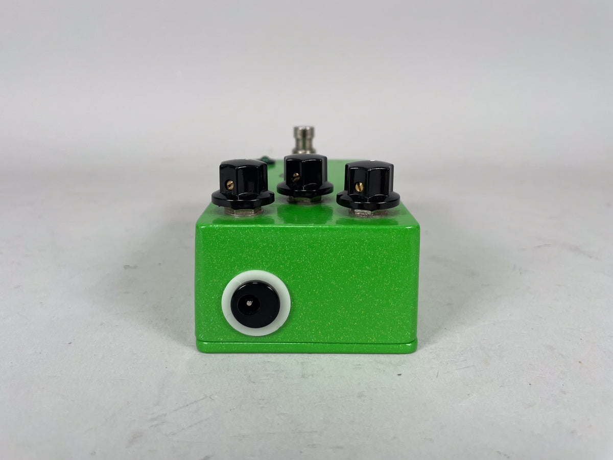 The sparkly green pedal is viewed from the front, showing three black control knobs on top and a black input jack on the front.