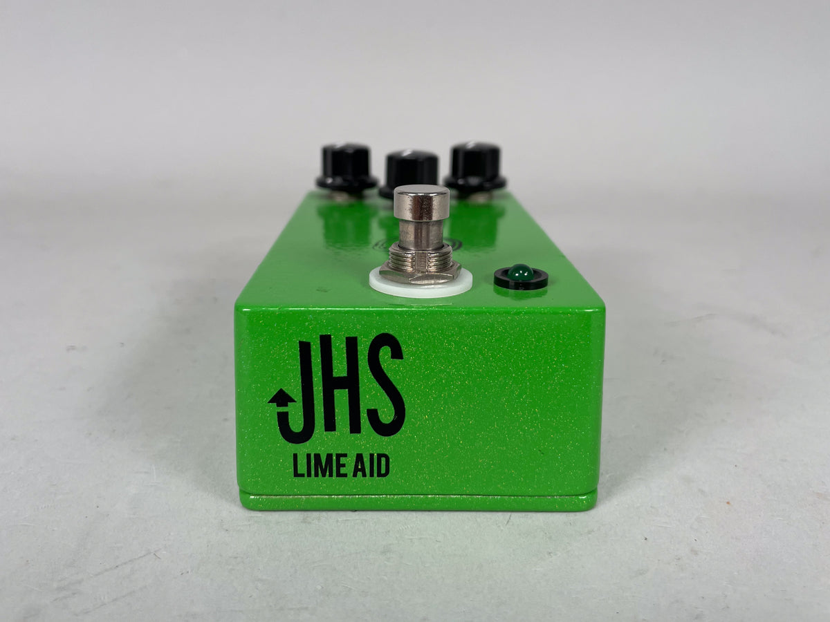 A bright green, glitter-finish effect pedal, viewed from the front, with a large footswitch, three black control knobs, and a green LED.
